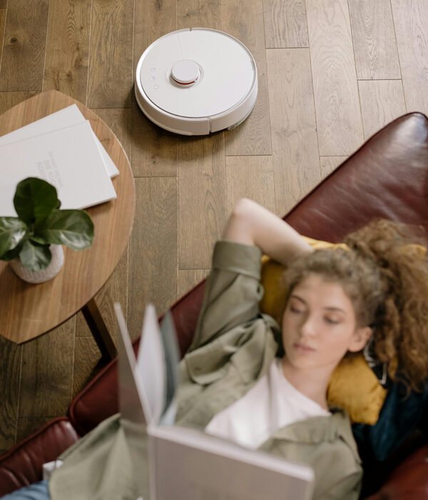 Girl relaxing with a book while a robot vacuum cleaner operates