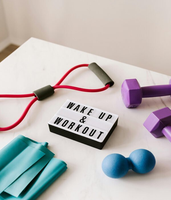 A sign in the middle of a table reads ‘Wake Up and Workout,’ surrounded by colourful exercise tools like dumbbells and resistance bands