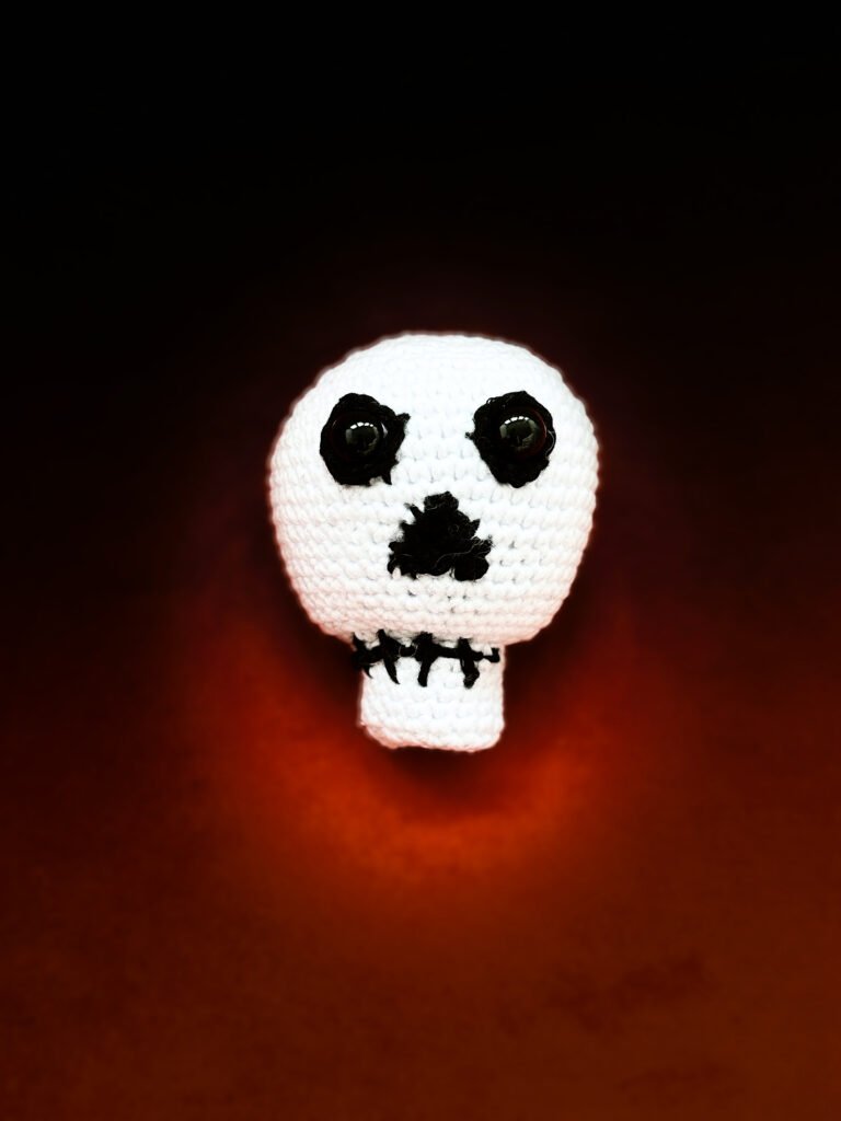 Crochet ideas: amigurumi skull which looks spooky but cute expression, set against a dark red moody background